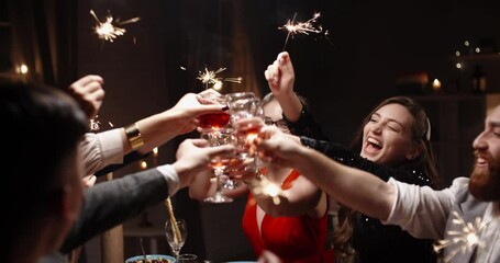 Group of multiethnic friends celebrating christmas together, cheering, smiling and holding burning sparklers at dinner party table - celebration, real people concept 4k footage - Powered by Adobe
