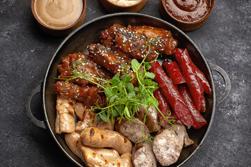 Meat set for beer, sausage, ribs, grilled wings, and three sauces, on a black background