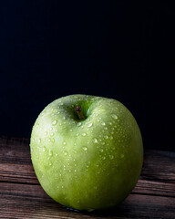 One green apple with water droplets against a black background.