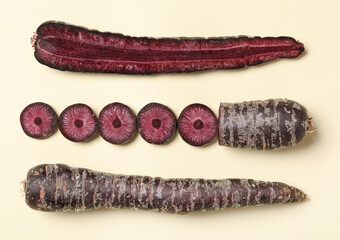 Whole and cut raw purple carrots on beige background, flat lay