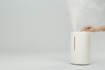 Woman using modern air humidifier on light grey background, closeup. Space for text
