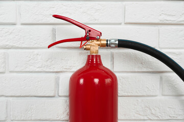 Naklejka premium Fire extinguisher near white brick wall, closeup