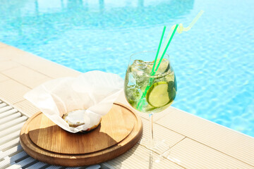 Glass of delicious mojito and brie cheese near swimming pool. Refreshing drink