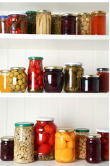 Jars of pickled fruits and vegetables on white wooden shelves