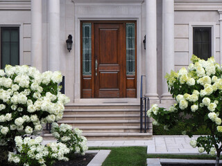 Elegant wooden front door with columns and flowering bush