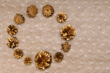 Delicate background of pine gilded cones, set in the form of a circular frame on the left, on knitted patterned canvas.