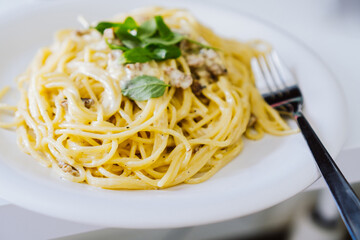 Homemade spaghetti Carbonara with pieces of bacon and basil. Fork on the side