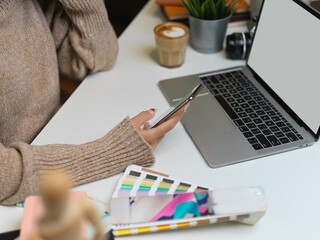 Fototapeta na wymiar Female designer in sweater using smartphone on office desk