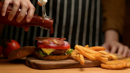 Female hand with a bottle of ketchup adding on fresh tasty bacon burger