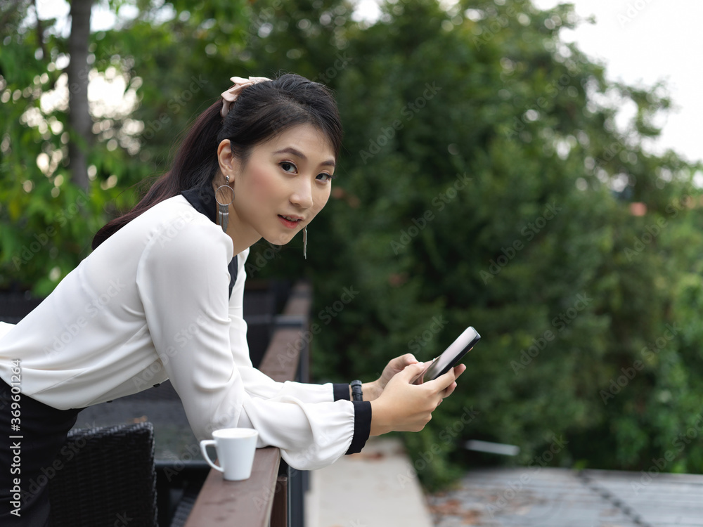 Wall mural portrait of businesswoman using smartphone while relaxed standing at balcony