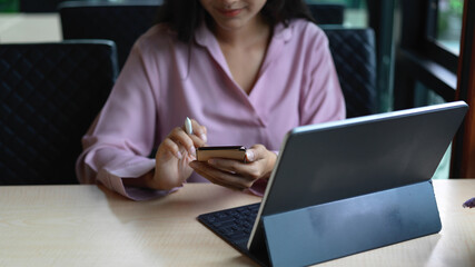 Businesswoman using smartphone while working with digital tablet on table in cafeteria