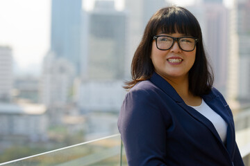 Happy young beautiful overweight Asian businesswoman against view of the city