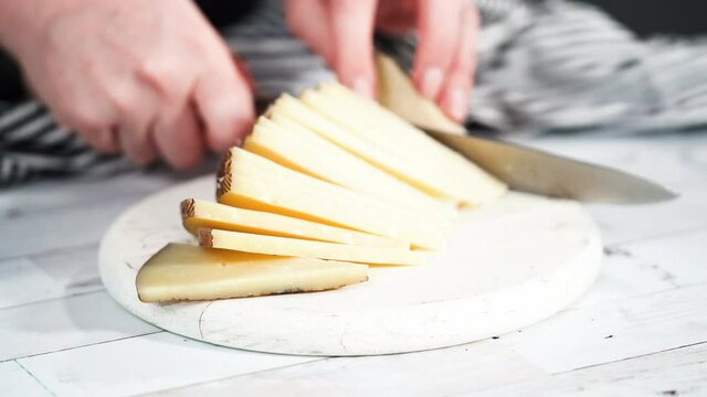 Step by step. Slicing a gourmet cheese on a white cutting board with a kitchen knife.