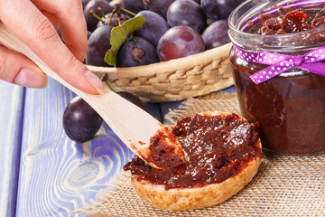 Hand with knife preparing fresh sandwiches with plum marmalade or jam, healthy sweet breakfast concept