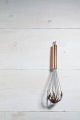 Steel hand whisk with chocolate sauce on white wooden background