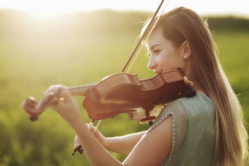 Romantic woman, girl with loose hair playing the violin. Sunset light in nature