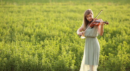 Romantic woman, girl with loose hair playing the violin. Sunset light in nature