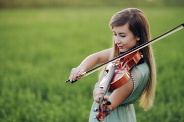 Romantic woman, girl with loose hair playing the violin. Sunset light in nature