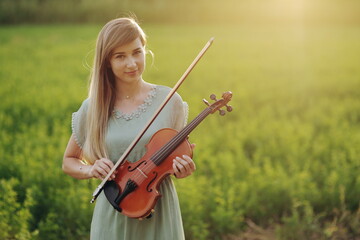Female musician violinist holding violin in her hands in sunset light