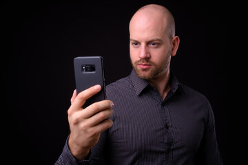Portrait of handsome bald bearded businessman using phone