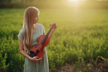 Female musician violinist holding violin in her hands in sunset light