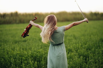 Happy musician violinist holding violin in her hands in sunset light