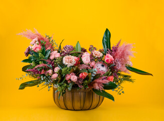 Brown wicker basket with a large flower arrangement of roses and peonies on a yellow background