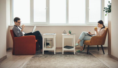 Side view photo of a caucasian couple with healthy habits working at the laptop while eating an apple and writing in book