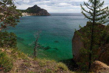 Rocky coast of lake Baikal in Peschanya bay with transparent water and clouds