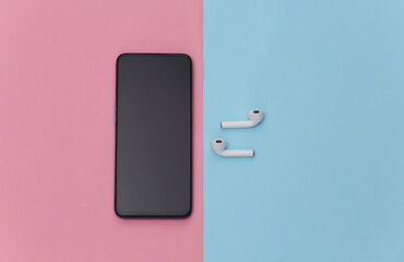 Modern smartphone with wireless earphones on blue pink pastel background. Top view. Flat lay