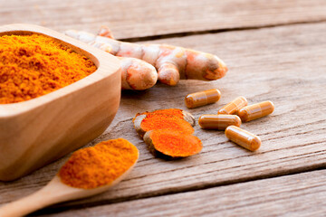 Turmeric powder herbal capsules and tumeric ground on  wood table background.