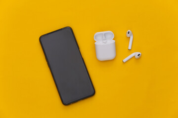 Modern smartphone and wireless earphones with charging case on yellow background. Top view. Flat lay