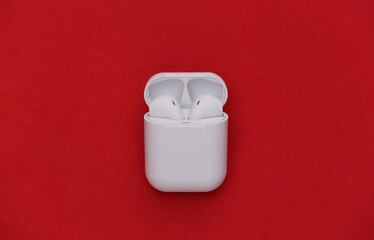 Modern wireless earphones with charging case on red background. Top view. Flat lay