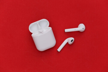 Modern wireless earphones with charging case on red background. Top view. Flat lay