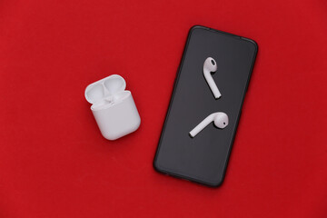 Modern smartphone and wireless earphones with charging case on red background. Top view. Flat lay
