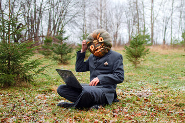 Halloween Scarecrow in a business suit with a laptop in his hands sitting in the forest