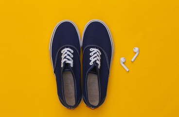 Sneakers shoes and wireless earphones on yellow background. Top view