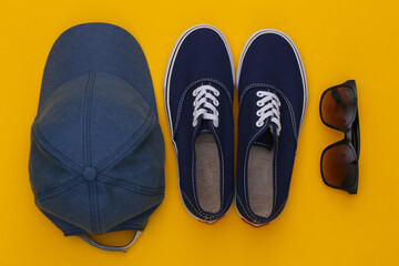 Cap and sunglasses, sneakers on yellow background. Top view. Flat lay