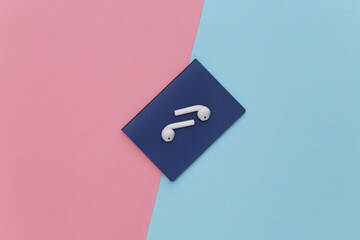 Passport and wireless earphones on a pink blue pastel background, travel concept. Top view