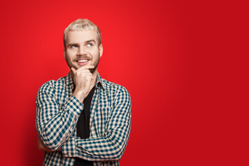 Caucasian man who got the idea and is posing aside on a red studio wall with free space touching his chin and smile