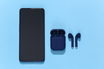 Smartphone and wireless bluetooth headphones or earbuds with charging case on bright blue...