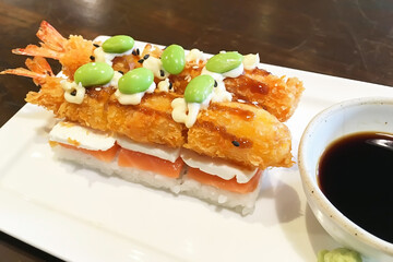 Japanese fusion food creative design with white rice, raw salmon sashimi on top with mayonnaise dressing on crispy fry shrimps and green beans serve with green fresh wasabi, soy sauce on white plate. 