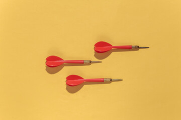 Three red plastic darts with metal tip on yellow bright background with deep shadow. Top view. Flat...