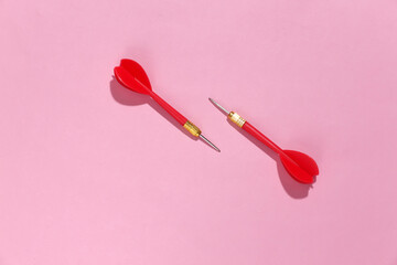 Two red plastic darts with metal tip on pink bright background with deep shadow. Top view. Flat lay
