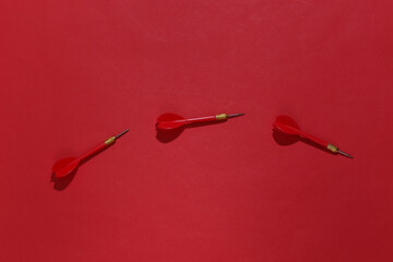 Three red plastic darts with metal tip on red bright background with deep shadow. Top view. Flat lay