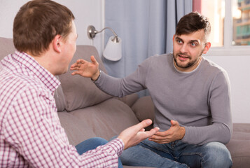 Happy male enjoying conversation with friend in cozy home interior on sofa