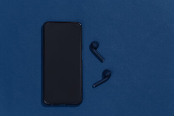 Smartphone and true wireless bluetooth headphones or earbuds on clasic blue background. Top view