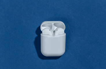 White true wireless bluetooth headphones or earbuds in charging case on classic blue background....