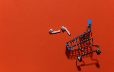 Mini shopping trolley with wireless bluetooth headphones on bright orange background. Top view