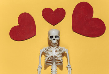 Skeleton and red decorative hearts on a bright yellow background. Valentine's day or halloween theme. Top view. Flat lay